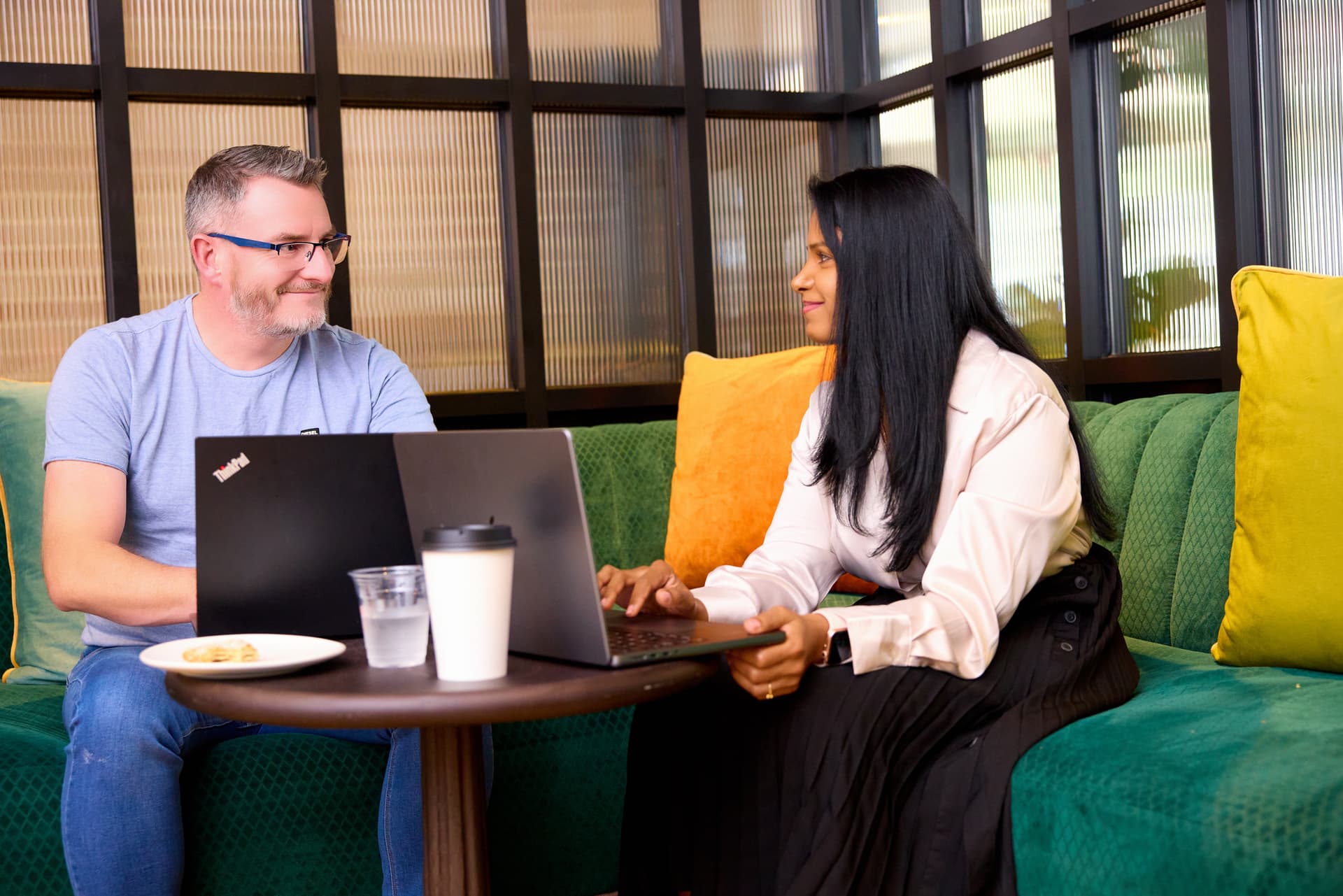 A man and a woman sit together with their laptops open