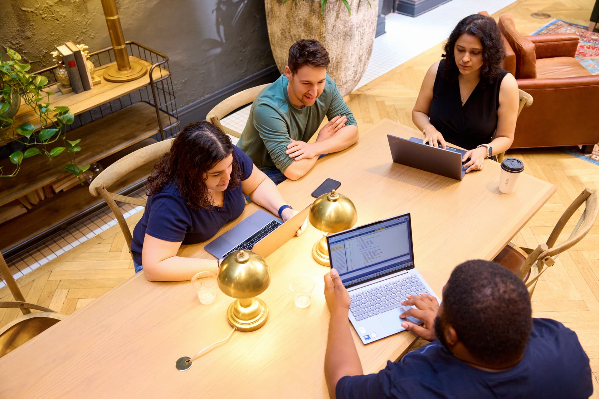 Four colleagues sit around a table with laptops open.